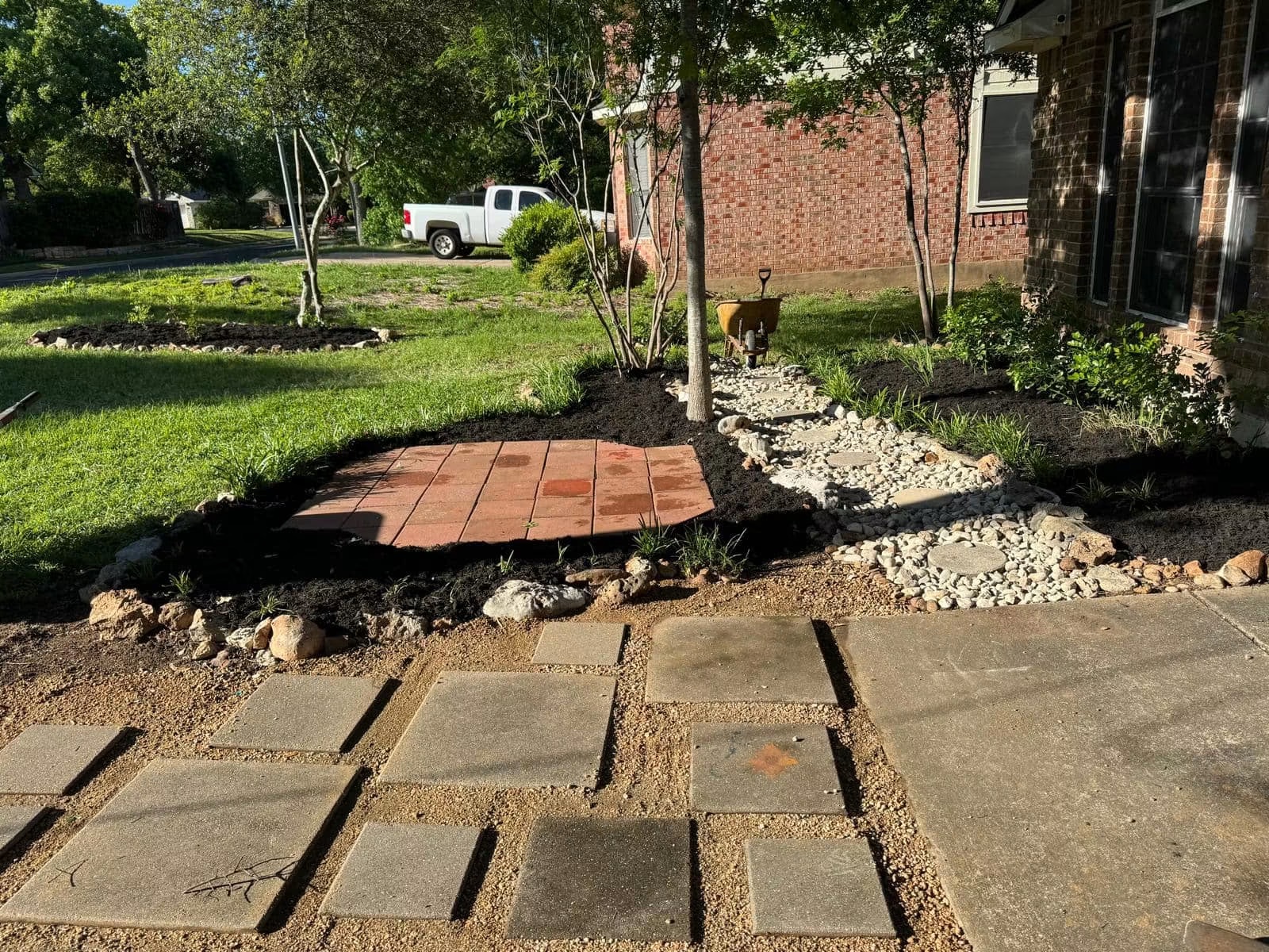 Residential front yard during paver, river-rock drainage, and garden-bed installation